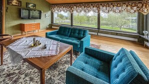 A living room with a wooden ceiling, a blue sofa, a wooden coffee table, and a TV on the wall.