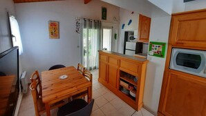 Uma cozinha compacta com armários de madeira, uma mesa de jantar com cadeiras, um frigorífico e um micro-ondas.