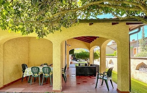 An outdoor patio with tables and chairs, covered by arches and a pergola, overlooking a street.
