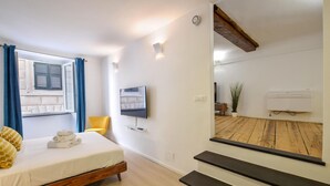 Quarto com cama, TV, planta em vaso e vista do assoalho de madeira.