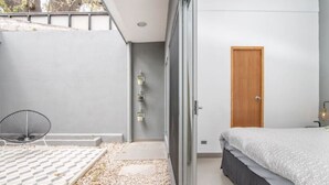 A modern bedroom with a bed, a chair, a wooden door, and a small balcony.