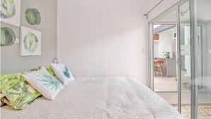 A bedroom with a large bed, a sliding glass door leading to a kitchen, and wall art.