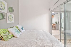 Relax in a serene bedroom with a large bed, framed botanical prints, and a sliding door to a dining area.