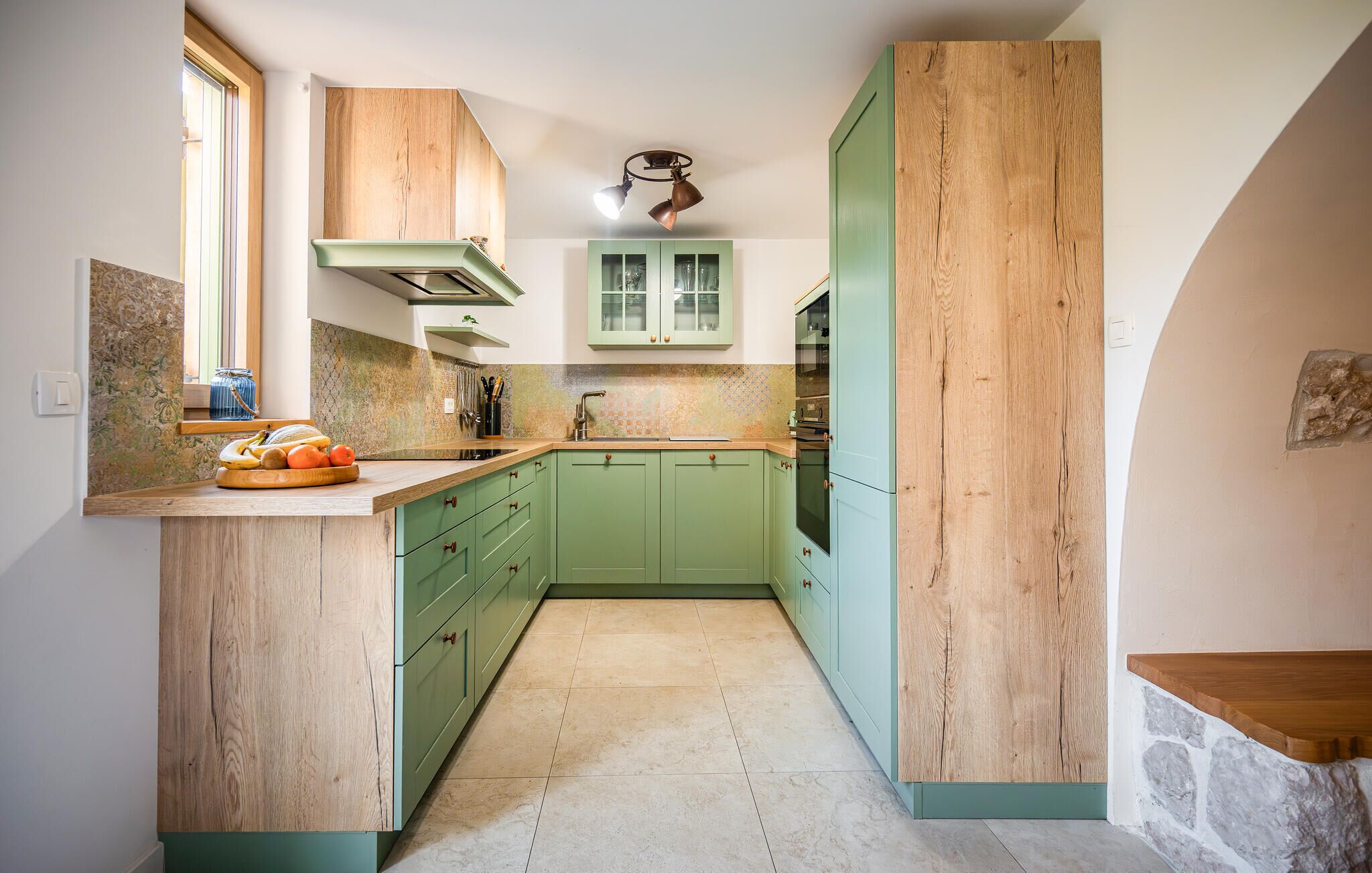 A compact kitchen with green cabinets, a wooden countertop, and a stone accent wall.