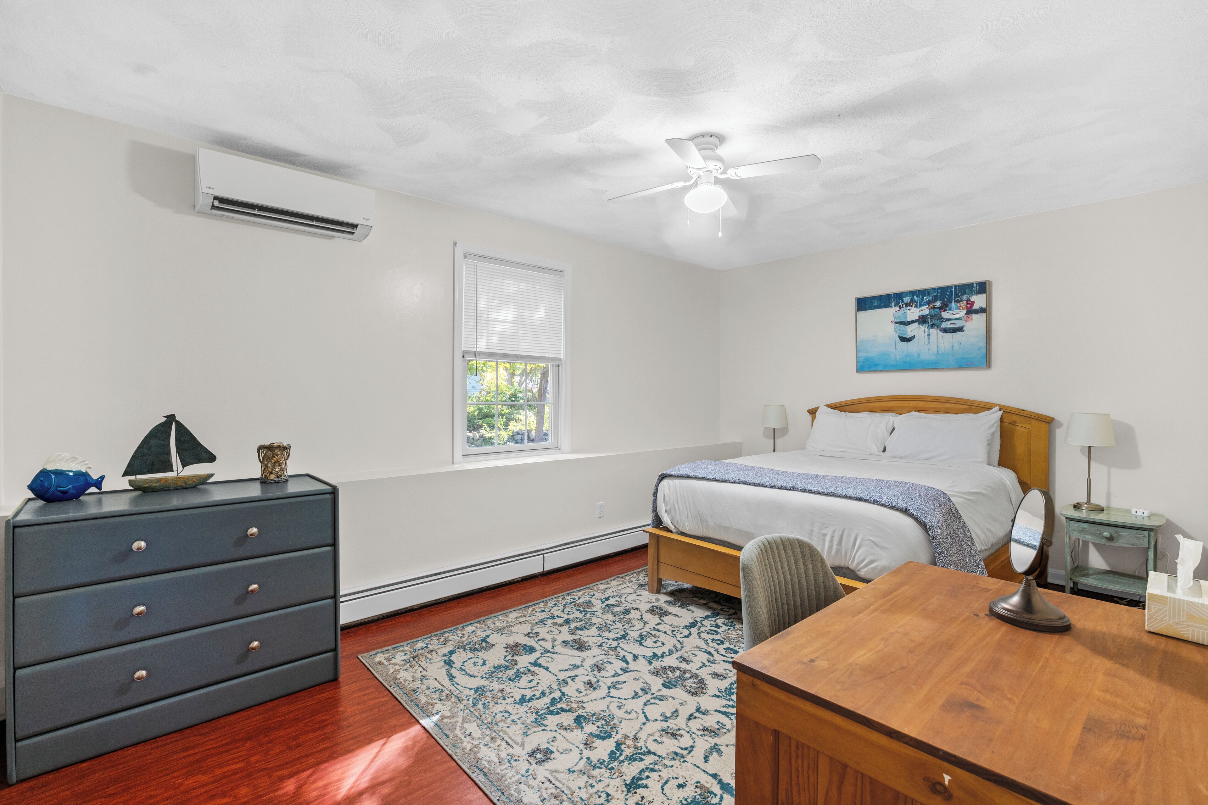A bedroom with a bed, a desk, a dresser, a ceiling fan, and a window with blinds.