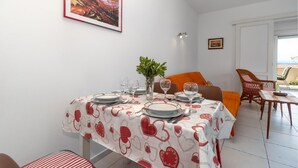 Ein Essbereich mit einem Tisch für zwei Personen, einem Bild an der Wand und Meerblick durch das Fenster.