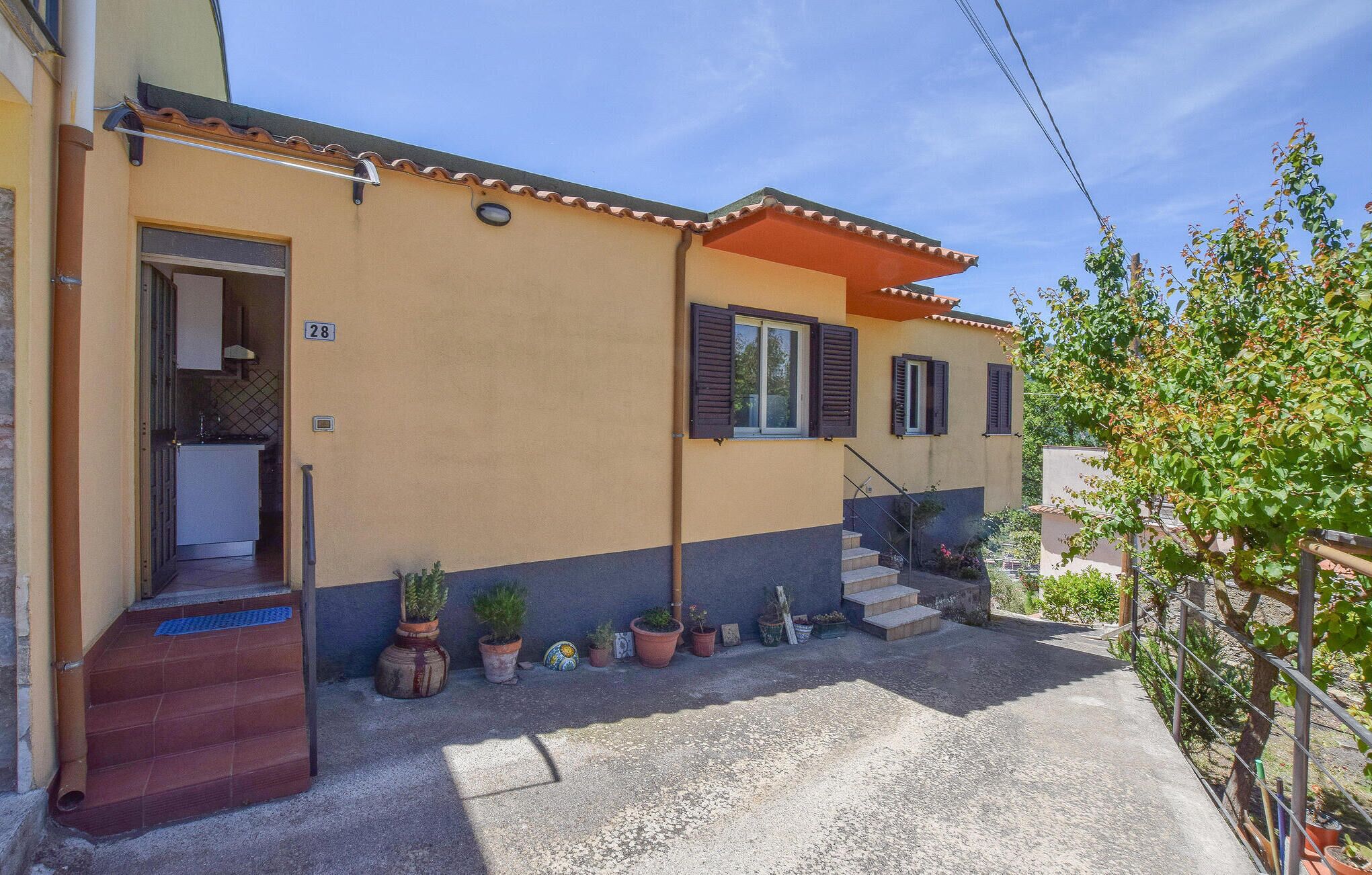 Una casa de dos pisos con fachada color beige, el número '28' visible, un pequeño jardín delantero con plantas en macetas y una escalera que conduce a la entrada.