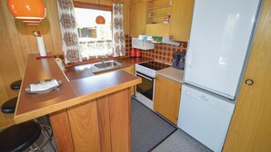 A compact kitchen with wooden cabinets, a sink, a stove, a microwave, and a refrigerator.