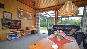 A cozy living room with a wooden table, a black leather sofa, and a large window offering a view of the outdoors.