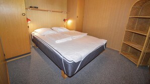 A neatly made bed in a room with wooden walls and a carpeted floor. There is a shelf with a few items on it and a small ladder leaning against the wall.