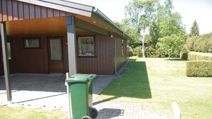 A building with a covered porch, a green trash bin, and a paved walkway.