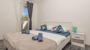 Een slaapkamer met een bed, twee kussens, een nachtkastje, een lamp en een raam met gordijnen.