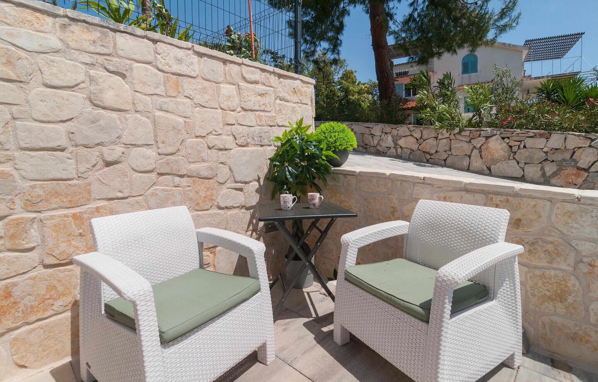 Un'area patio con due poltrone in vimini bianco e un tavolino, circondata da muri in pietra e piante in vaso.