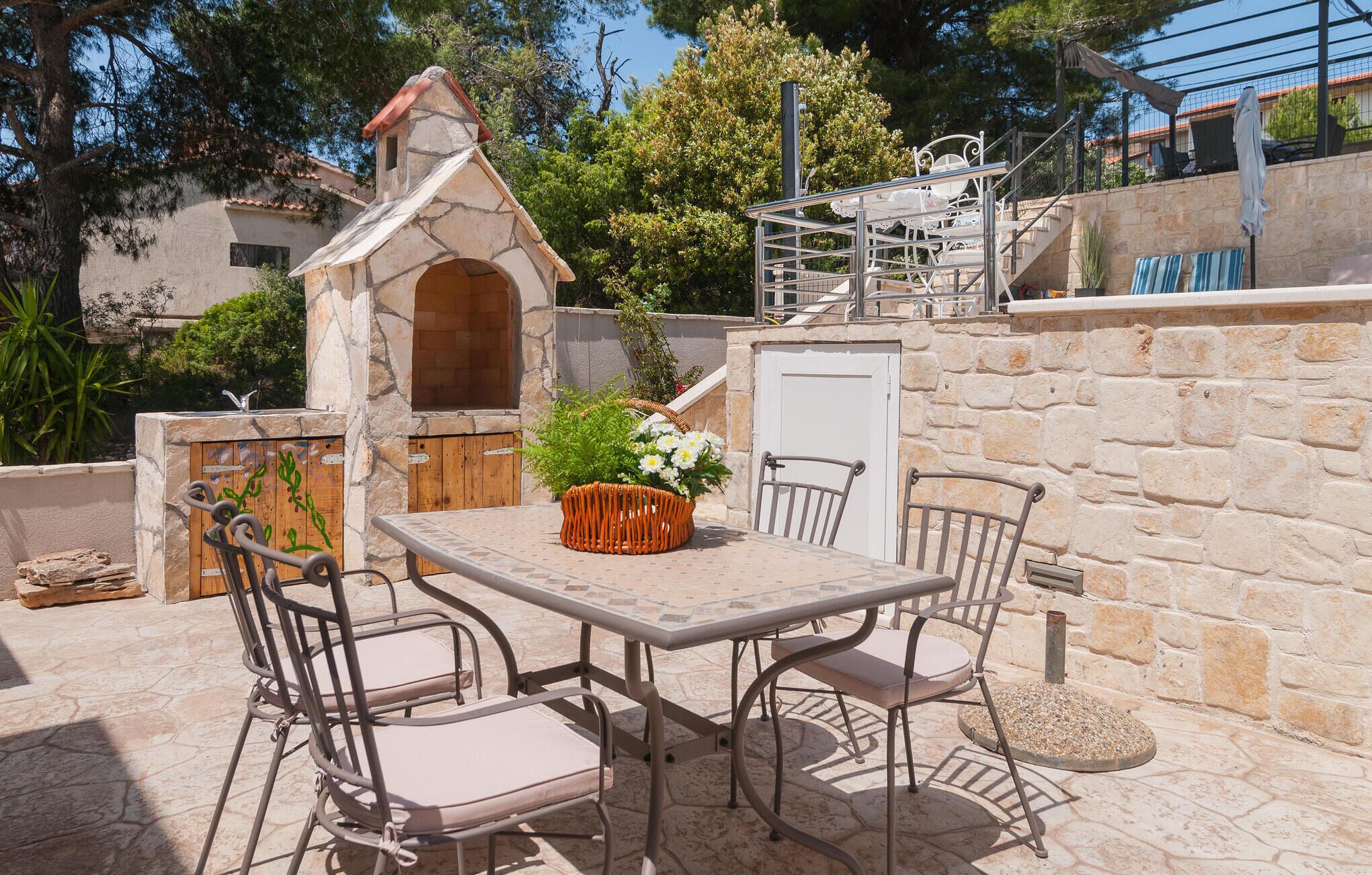 An outdoor patio with a stone wall, a metal table, four chairs, and a small stone oven.