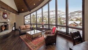 A spacious living room with a fireplace, leather furniture, and large windows offering a view of a snowy mountain town. - Stay on Forest Road! Walk to Lionshead! (Vail)