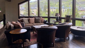 A spacious living room with a large window offering a view of a mountainous landscape and residential buildings. - Stay on Forest Road! Walk to Lionshead! (Vail)