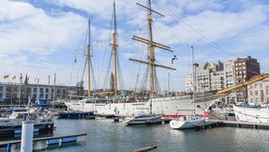 Ein Yachthafen mit mehreren Segelbooten an den Liegeplätzen, ein Gebäude mit mehreren Flaggen und ein modernes Gebäude mit geneigtem Dach.