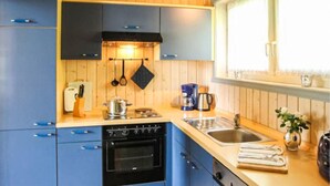 Eine Küche mit blauen Schränken, einem schwarzen Backofen, einer Spüle und einem Fenster mit Vorhängen.