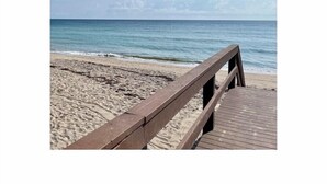 A wooden boardwalk leading to a sandy beach with a calm sea and a clear sky.