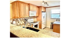 A kitchen with wooden cabinets, a granite countertop, a white stove, a microwave, and a refrigerator.
