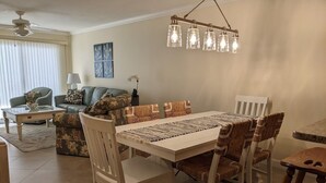 A dining area with a white table, six chairs, and a hanging light fixture.
