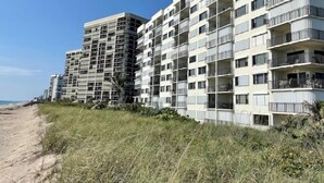 A beachfront hotel with multiple floors, balconies, and a sandy beach in the background.