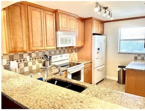 A kitchen with wooden cabinets, a granite countertop, a white stove, a microwave, and a refrigerator.