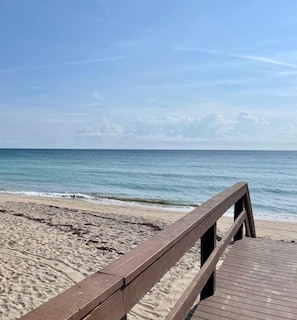 A wooden boardwalk leading to a sandy beach with a calm sea and a clear sky.