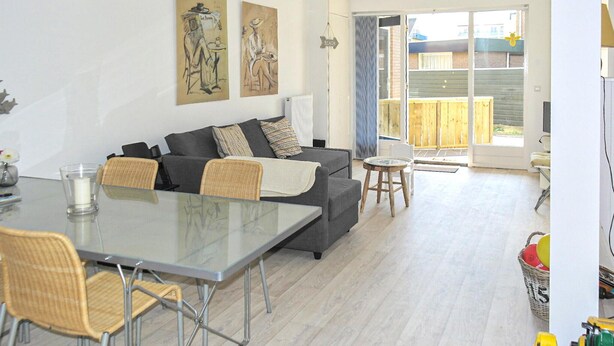 Ein modernes Wohnzimmer mit grauem Sofa, einem Glastisch, Korbstühlen und Kunstwerken an den Wänden.