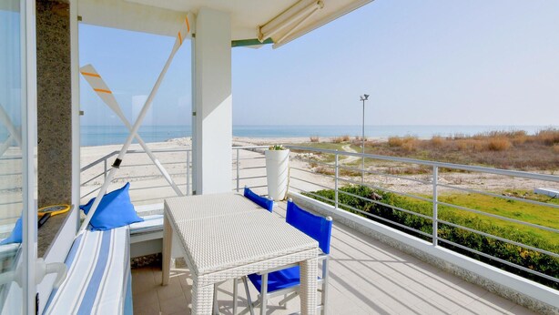 Un balcon avec une table et des chaises en osier, donnant sur une plage.