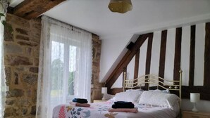 Un dormitorio con pared de piedra, cama con ropa de cama floral, techo de madera y mesita de noche.