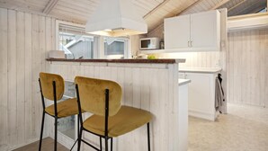 Une cuisine avec des murs en bois, un plan de travail blanc et deux chaises jaunes.
