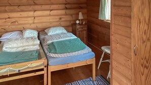 Una habitación tipo cabaña con dos literas, una mesita de noche de madera con lámpara, y una ventana con cortina.