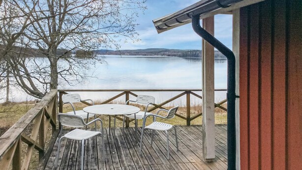 Una terraza de madera con mesa y sillas frente a un lago tranquilo.