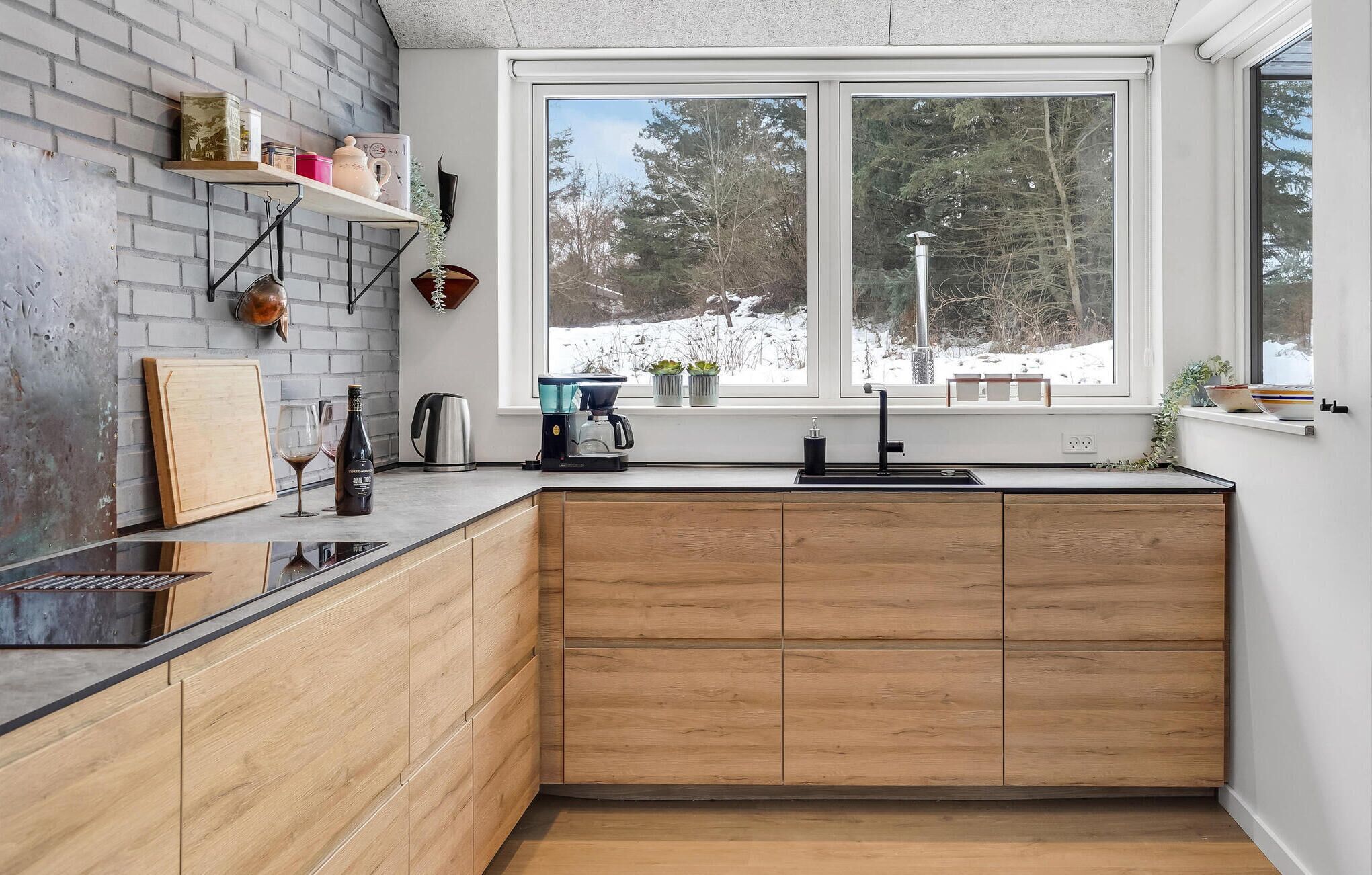 Una cocina compacta con armarios de madera, una encimera negra y una ventana que ofrece vistas a un paisaje nevado.