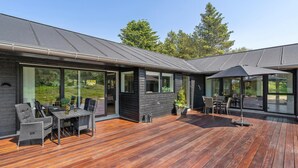 Une maison moderne dotée d’une terrasse en bois, de grandes portes-fenêtres coulissantes et de mobilier d’extérieur.