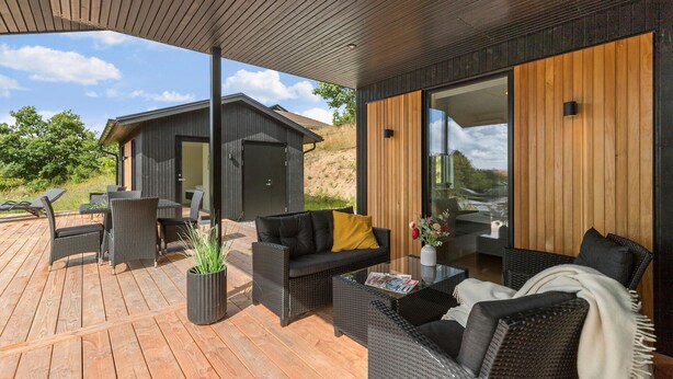 A modern outdoor patio with wicker furniture, a wooden deck, and a view of a hillside.