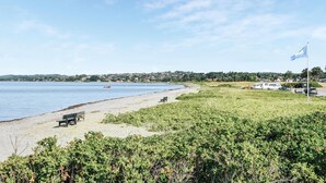 A beach with a bench, a flag, and a row of houses in the background.