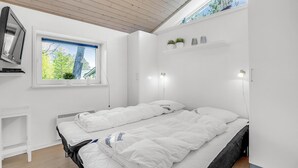Ett modernt sovrum med en säng, en tv, ett fönster och en hylla med växter.