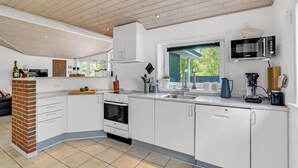 Ett modernt kök med vita skåp, en tegelvägg som accent, en inbyggd ugn och ett fönster med utsikt över grönområden.