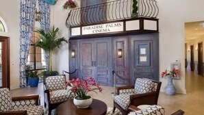 A lobby with a cinema named 'Paradise Palms' featuring a wooden ceiling, patterned chairs, and a decorative railing.