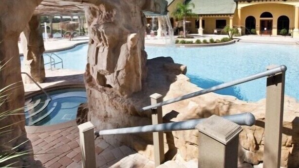 A pool area with a rock formation and a building in the background.