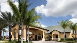 A hotel with a Mediterranean architectural style, featuring a central courtyard with palm trees and a paved walkway.