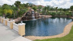 A landscaped area with a pond, a waterfall, and a paved walkway.