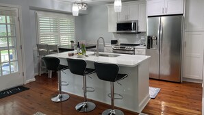 A modern kitchen with white cabinetry, stainless steel appliances, and a central island with bar stools. - Private home in Mt. Pleasant, SC Vacation Rental 10 min drive to the beach. (Mount Pleasant)