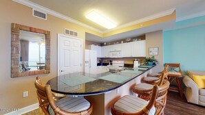 A modern kitchen with a central island, white cabinets, and a dining area with wicker chairs. - Beachfront, 24th Floor (Panama City Beach)
