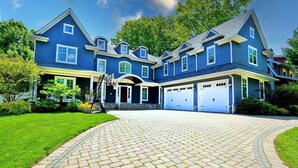 Une grande maison à deux étages, dotée d’un garage, d’une allée et d’une pelouse bien entretenue.