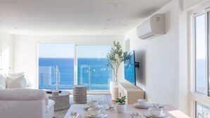 A modern living room with a dining area, large windows with a view of the sea, and a flat-screen TV mounted on the wall. - Oceans Views Zen Retreat | 6 Min Walk to Beach | Dolphin Spotting | Pet OK (Malibu)