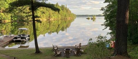 A lakeside deck with a dock, chairs, and a fire pit.