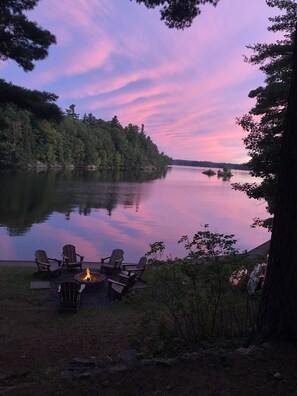 A lakeside view with a fire pit and Adirondack chairs. - Lakefront Cottage near Adirondacks, Pontoon Boat, Sunroom, 2 Kayaks & Canoe (Hermon)